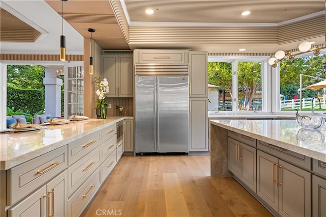 kitchen with gray cabinetry, light stone countertops, built in appliances, pendant lighting, and light wood-type flooring