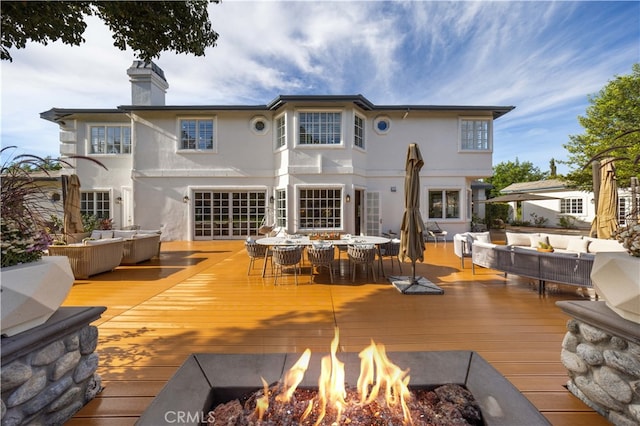 rear view of property with a wooden deck and an outdoor living space with a fire pit