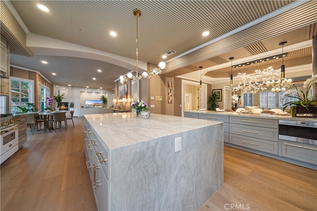 kitchen with gray cabinetry, a spacious island, light wood-type flooring, light stone countertops, and decorative light fixtures