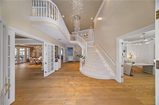 foyer with a notable chandelier, wood-type flooring, a towering ceiling, and french doors