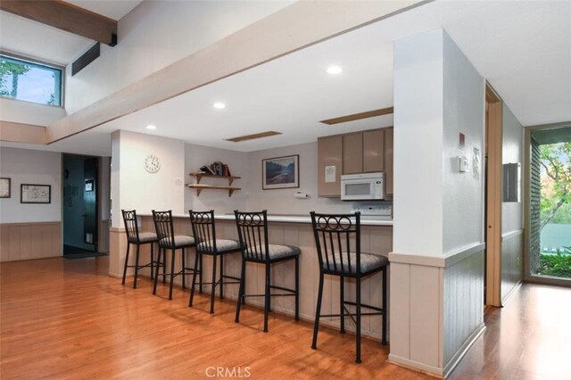 kitchen featuring gray cabinetry, beamed ceiling, kitchen peninsula, a breakfast bar, and light wood-type flooring