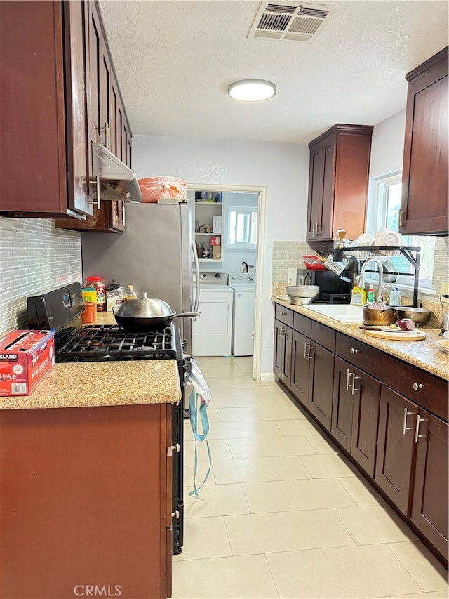 kitchen featuring decorative backsplash, washer and dryer, light stone countertops, stainless steel range with gas stovetop, and sink