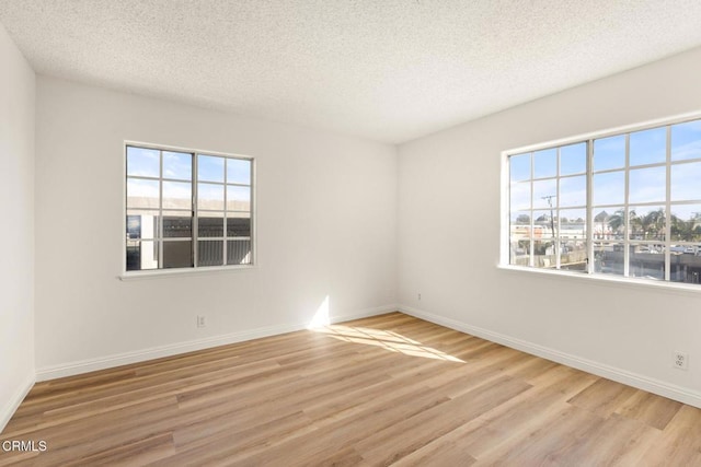 empty room featuring plenty of natural light, wood finished floors, baseboards, and a textured ceiling