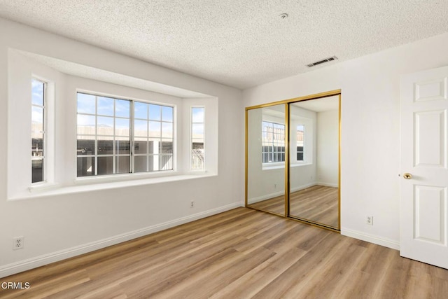 unfurnished bedroom featuring visible vents, a textured ceiling, wood finished floors, a closet, and baseboards