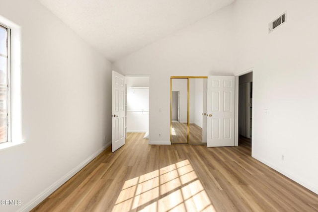 unfurnished bedroom featuring visible vents, baseboards, light wood-style floors, and high vaulted ceiling