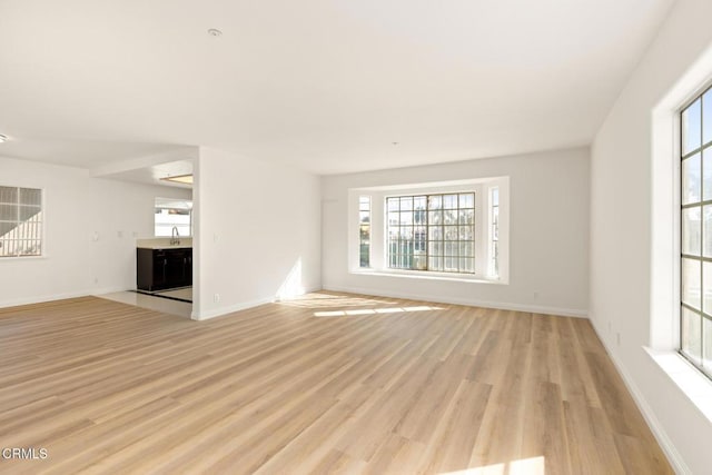 unfurnished living room with light wood finished floors, baseboards, and a sink