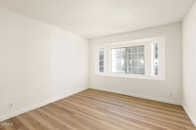 spare room with light wood-style floors, baseboards, and a textured ceiling