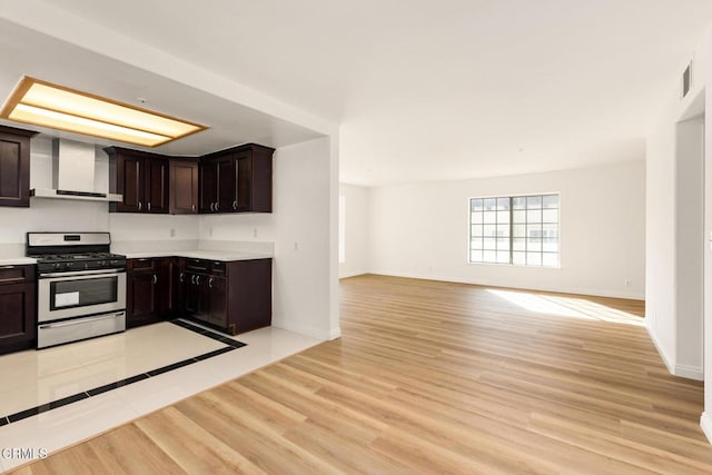 kitchen featuring light countertops, wall chimney range hood, gas stove, and light wood finished floors