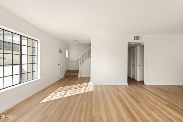 unfurnished living room with stairway, baseboards, visible vents, and light wood finished floors