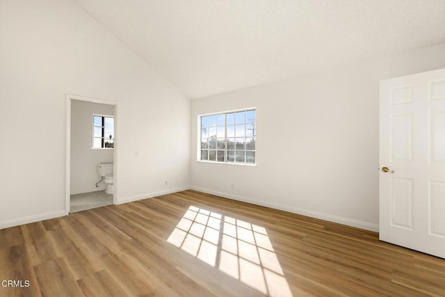 unfurnished bedroom with baseboards, high vaulted ceiling, wood finished floors, and ensuite bathroom