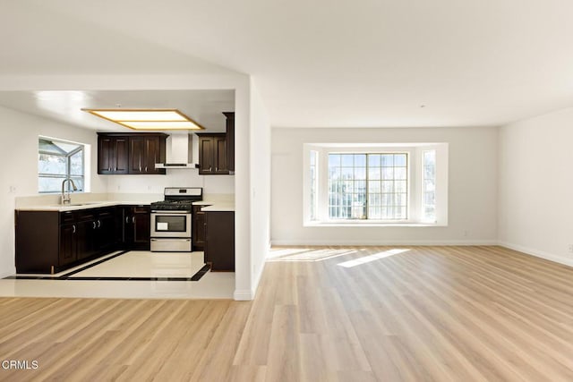 kitchen featuring light wood finished floors, light countertops, stainless steel gas stove, wall chimney exhaust hood, and a sink