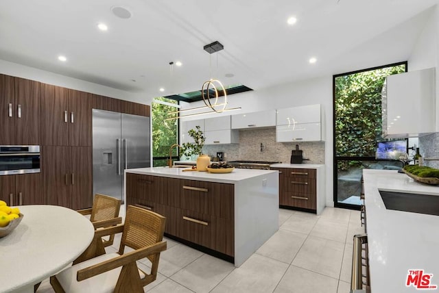 kitchen with stainless steel appliances, decorative light fixtures, decorative backsplash, a center island with sink, and white cabinets