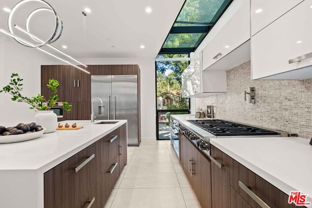 kitchen with a skylight, sink, stainless steel appliances, tasteful backsplash, and white cabinets