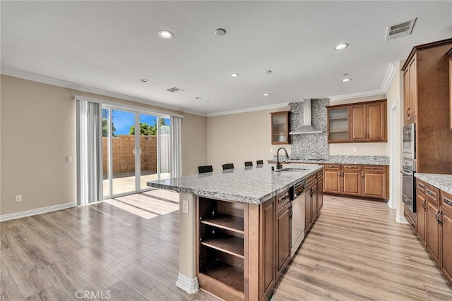 kitchen with appliances with stainless steel finishes, a kitchen island with sink, light wood-type flooring, wall chimney exhaust hood, and sink