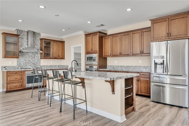 kitchen with wall chimney range hood, a breakfast bar area, light hardwood / wood-style flooring, stainless steel appliances, and a center island with sink