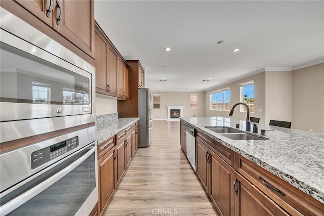 kitchen with stainless steel appliances, ornamental molding, sink, light stone countertops, and light hardwood / wood-style floors