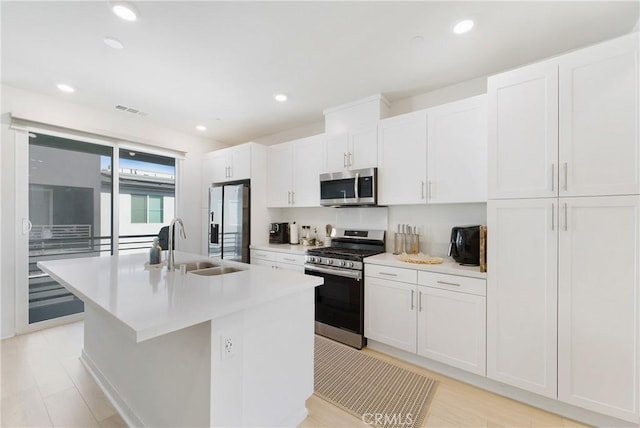 kitchen with white cabinets, appliances with stainless steel finishes, sink, and an island with sink