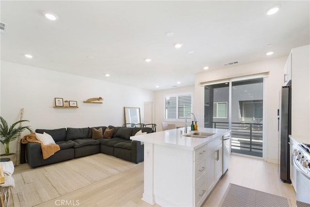 kitchen featuring light wood-type flooring, stainless steel appliances, sink, white cabinetry, and an island with sink