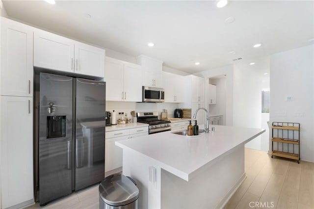 kitchen featuring white cabinets, sink, light wood-type flooring, an island with sink, and stainless steel appliances