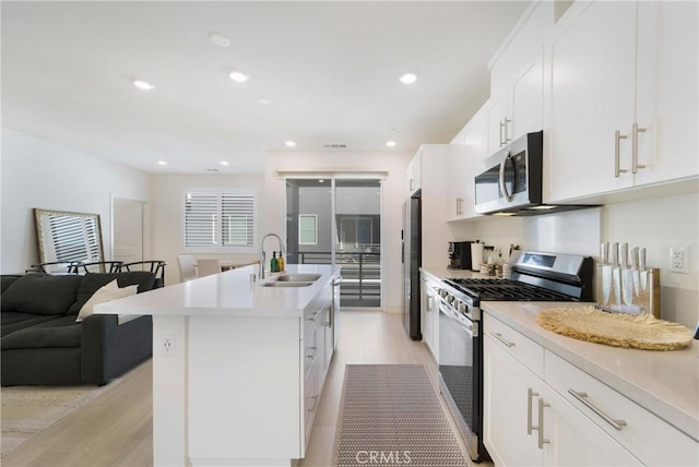 kitchen with white cabinets, stainless steel appliances, a kitchen island with sink, and sink