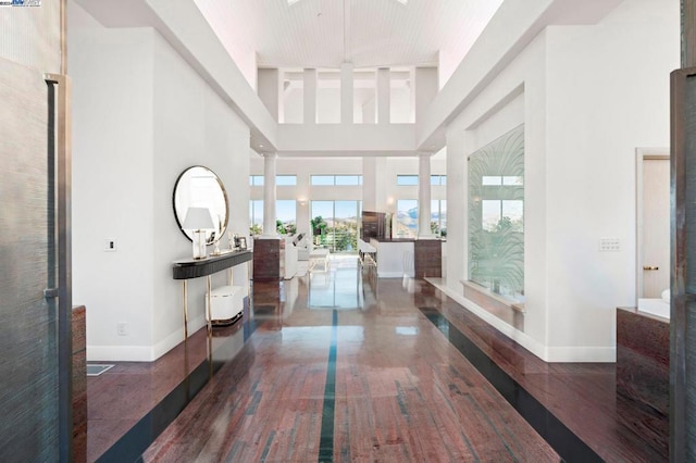 hall with decorative columns, a towering ceiling, and dark wood-type flooring