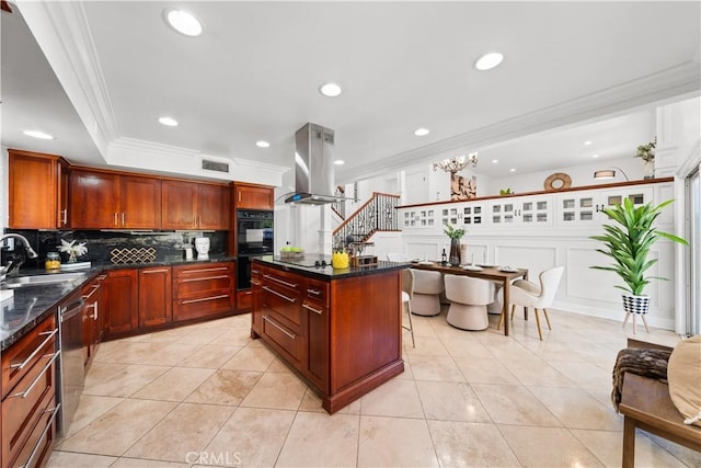 kitchen with sink, black double oven, ornamental molding, tasteful backsplash, and island range hood