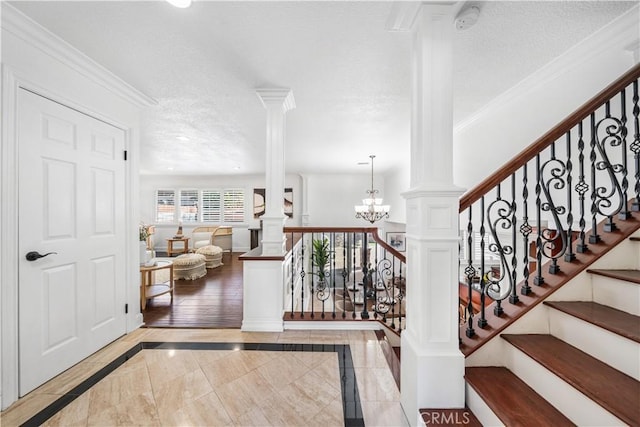 stairway featuring a chandelier, a textured ceiling, decorative columns, and ornamental molding