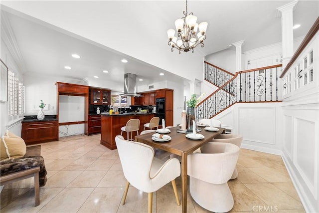 tiled dining area with a high ceiling, decorative columns, an inviting chandelier, and ornamental molding