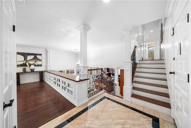 staircase with decorative columns, wood-type flooring, and a textured ceiling