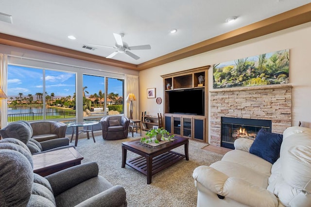 living room with ceiling fan, a stone fireplace, a water view, and light carpet