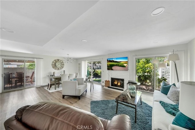 living room with a fireplace, a chandelier, light hardwood / wood-style flooring, and plenty of natural light