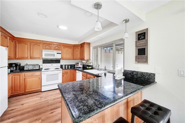 kitchen with hanging light fixtures, a sink, dark stone countertops, white appliances, and a peninsula