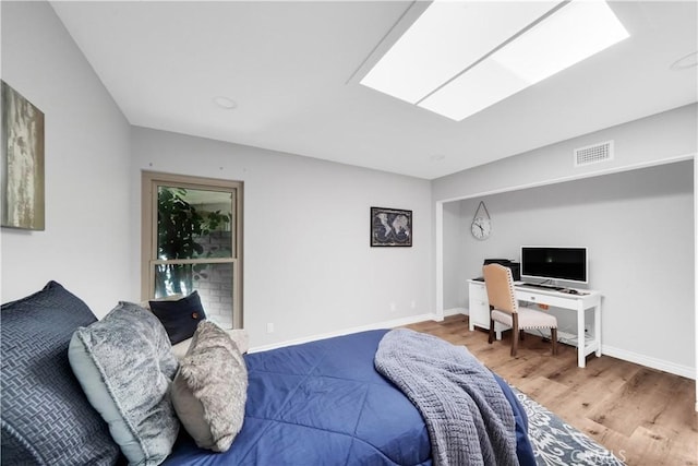 bedroom with a skylight, visible vents, baseboards, and wood finished floors