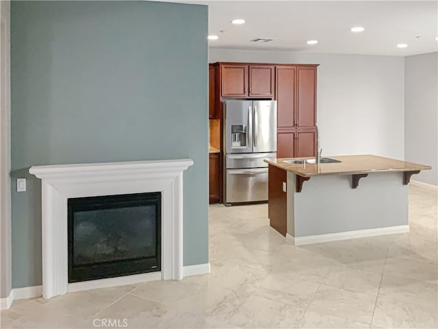 kitchen featuring sink, a kitchen breakfast bar, a center island with sink, and stainless steel fridge