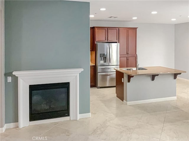 kitchen with a kitchen bar, sink, a kitchen island with sink, and stainless steel fridge