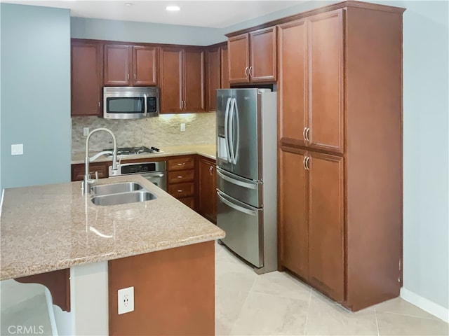 kitchen featuring tasteful backsplash, light stone countertops, appliances with stainless steel finishes, sink, and a breakfast bar area