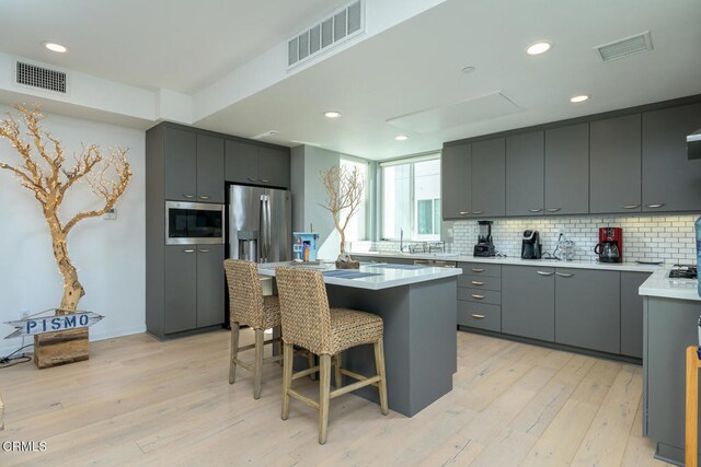 kitchen featuring appliances with stainless steel finishes, a center island, light wood-type flooring, and gray cabinets