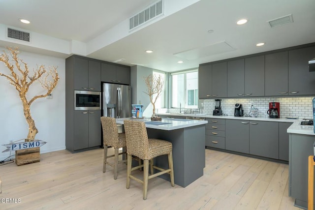 kitchen with gray cabinetry, appliances with stainless steel finishes, a kitchen bar, and visible vents