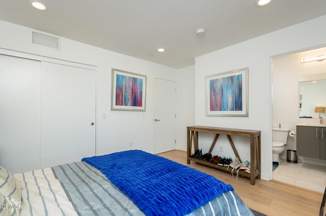 bedroom featuring a closet, light hardwood / wood-style floors, ensuite bathroom, and sink