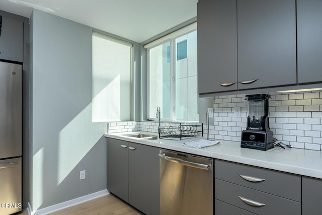 kitchen with appliances with stainless steel finishes, sink, light hardwood / wood-style floors, gray cabinets, and decorative backsplash