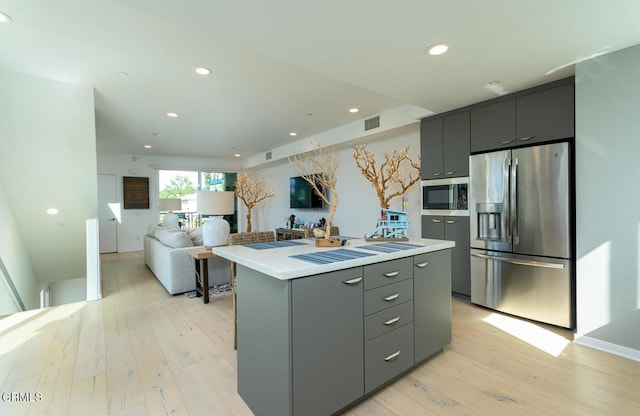 kitchen featuring gray cabinetry, appliances with stainless steel finishes, light hardwood / wood-style flooring, and a kitchen island with sink