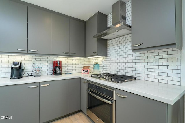 kitchen with wall chimney range hood, appliances with stainless steel finishes, light countertops, gray cabinets, and light wood-type flooring