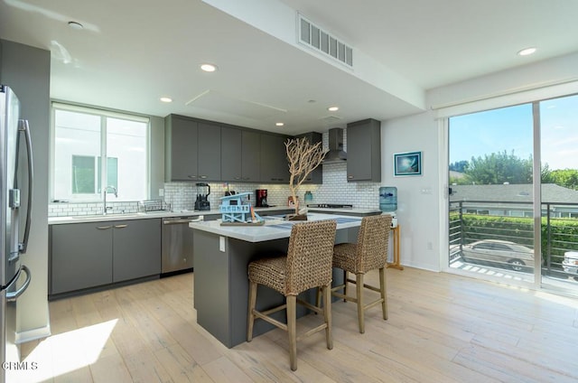 kitchen with wall chimney range hood, gray cabinets, visible vents, appliances with stainless steel finishes, and light wood-type flooring