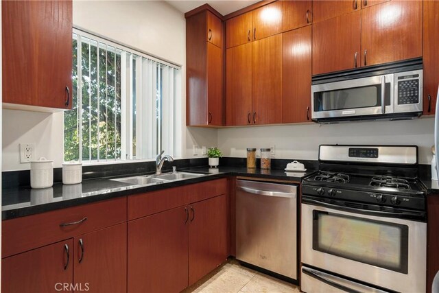 kitchen featuring light tile patterned floors, stainless steel appliances, dark stone counters, and sink