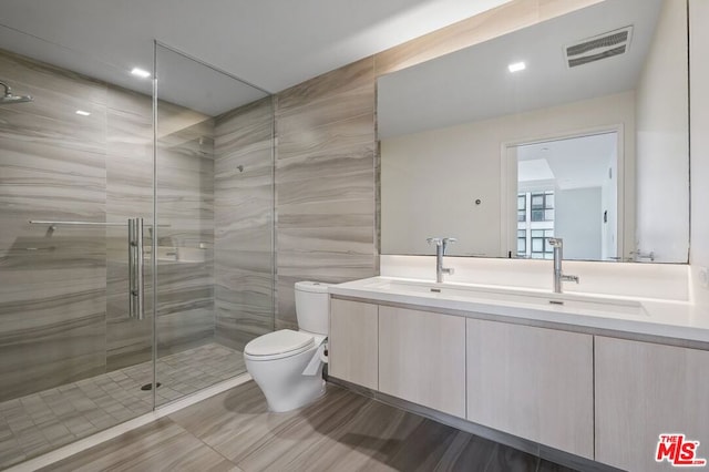 bathroom featuring vanity, a shower with shower door, tile walls, and toilet