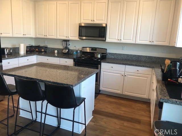 kitchen with a breakfast bar area, dark wood-type flooring, stainless steel appliances, dark stone counters, and white cabinetry