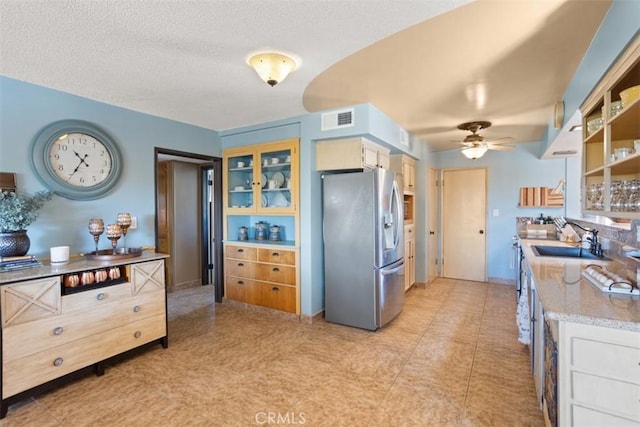 kitchen with white cabinets, ceiling fan, stainless steel fridge, and sink