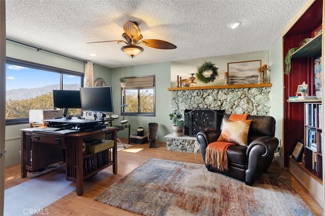 office space with wood-type flooring, a fireplace, ceiling fan, and a textured ceiling