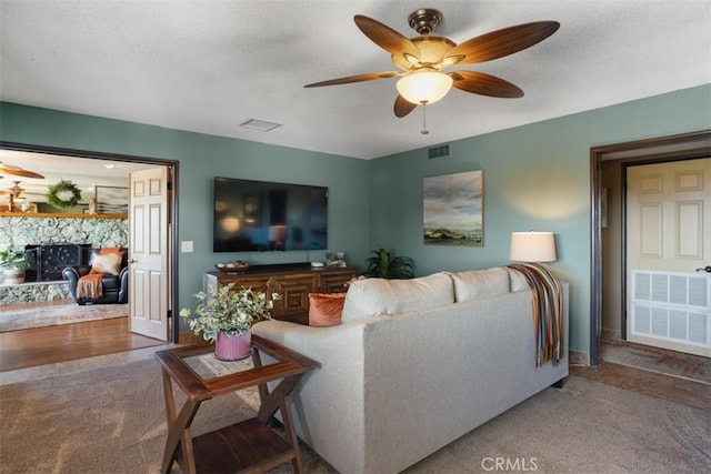 carpeted living room featuring a fireplace, a textured ceiling, and ceiling fan