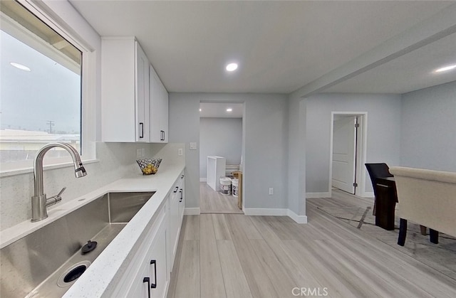 kitchen with white cabinets, backsplash, light wood-type flooring, and sink